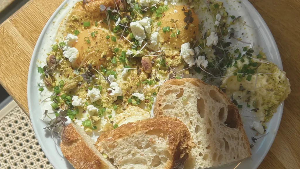 Pyszne śniadanie w restauracji Przesada w Krakowie – kremowe jajka z masłem chili i pistacjami oraz chrupiące pieczywo.